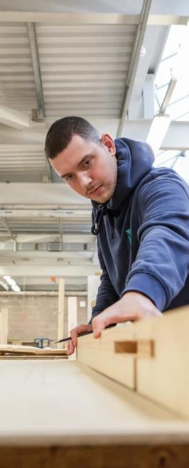 A joinery student carefully measuring and marking timber in a brightly lit woodworking workshop, focused on accuracy and precision. A joinery student carefully measuring and marking timber in a brightly lit woodworking workshop, focused on accuracy and precision.
